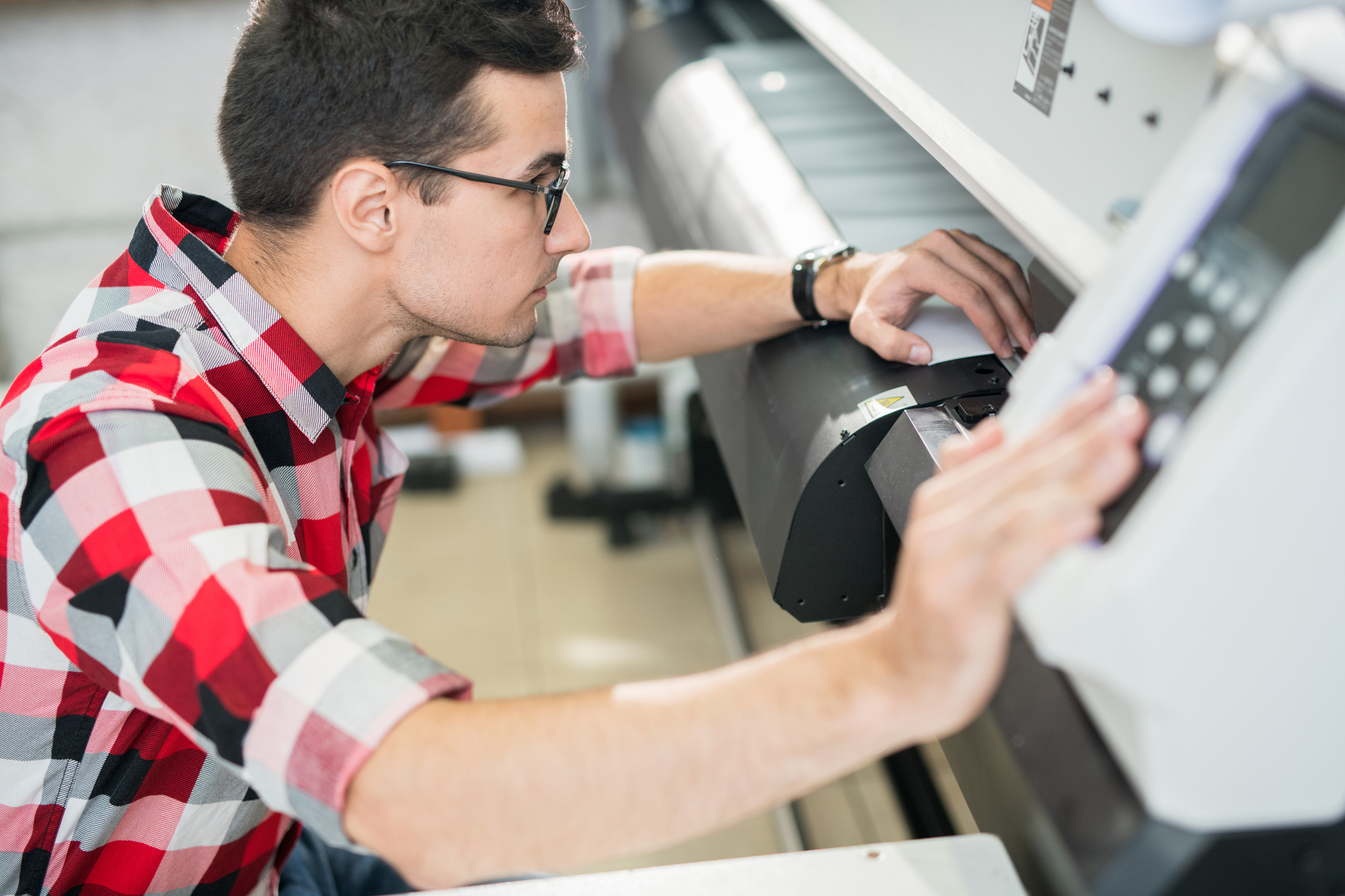 Serious thoughtful handsome young engineer in shirt examining wide format printer while holding inspection in printing house