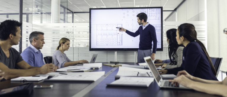 Architect standing in front of a presentation screen and pointing to it while explaining details to the audience.