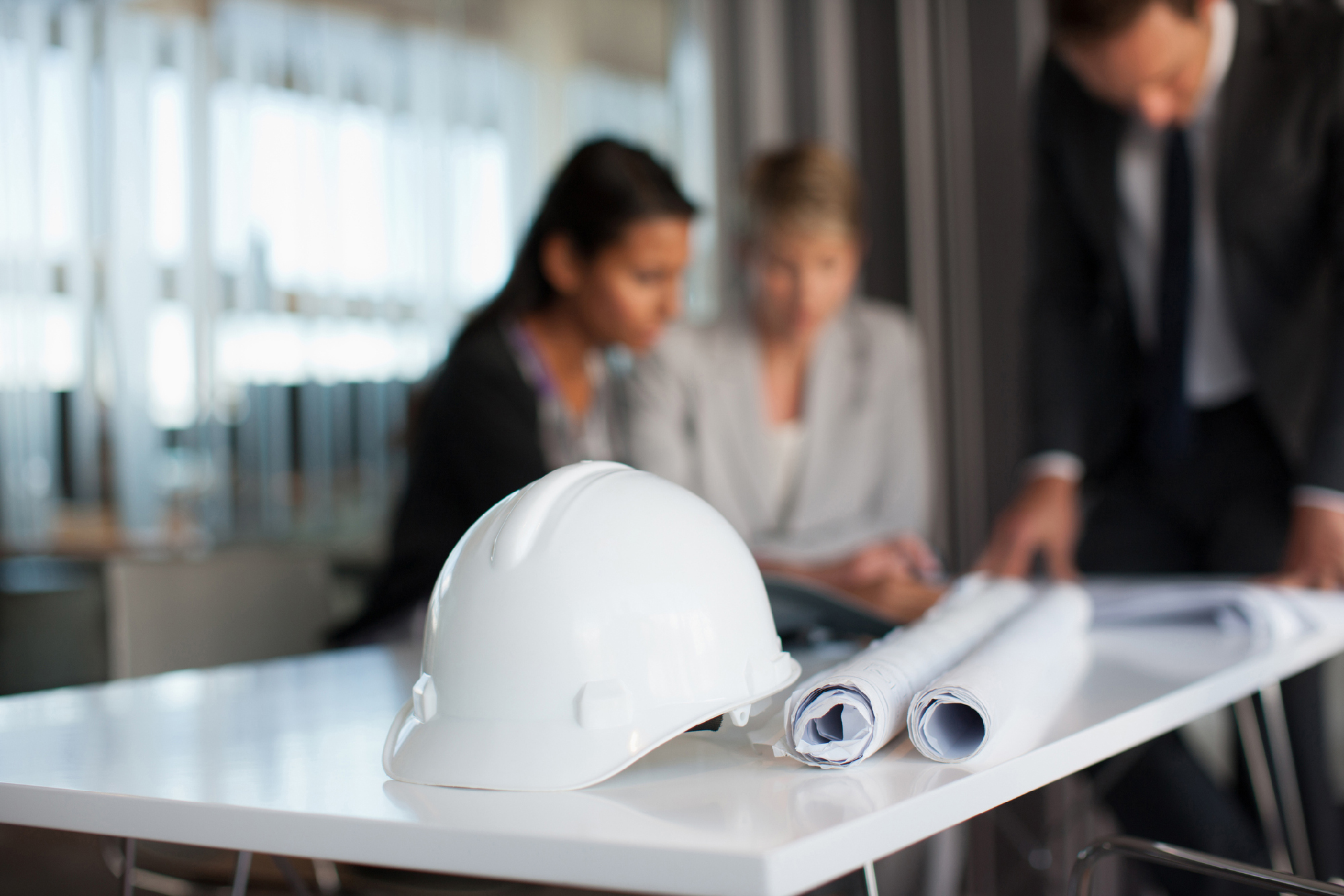 Hard hat in focus with Business people reviewing blueprints in conference room