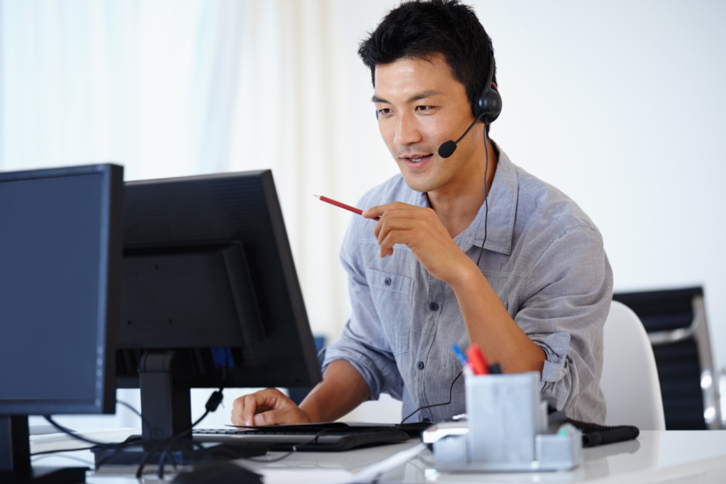 Asian man using a computer and talking on a headset