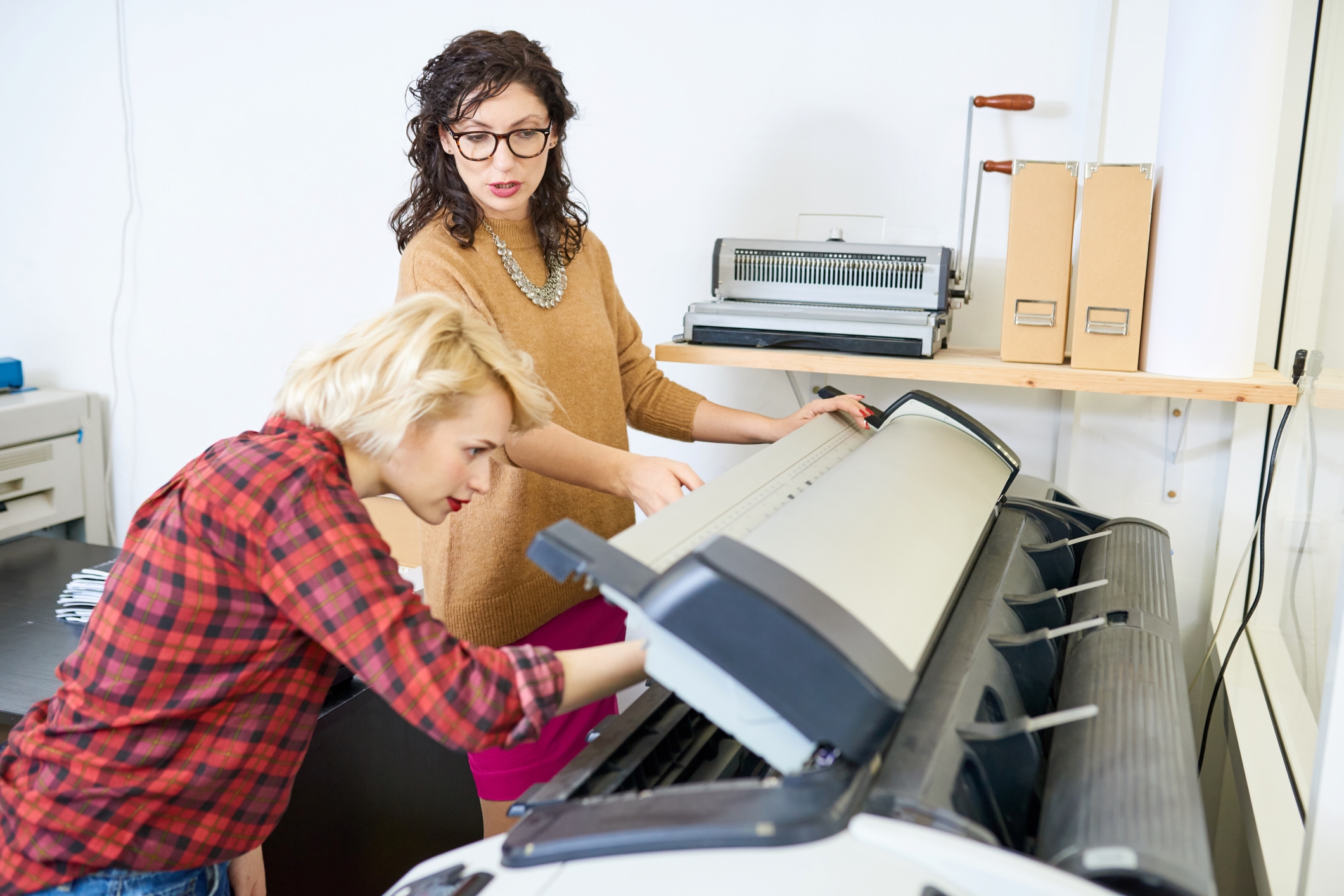 Two women stand over a wide format printer assessing outputs