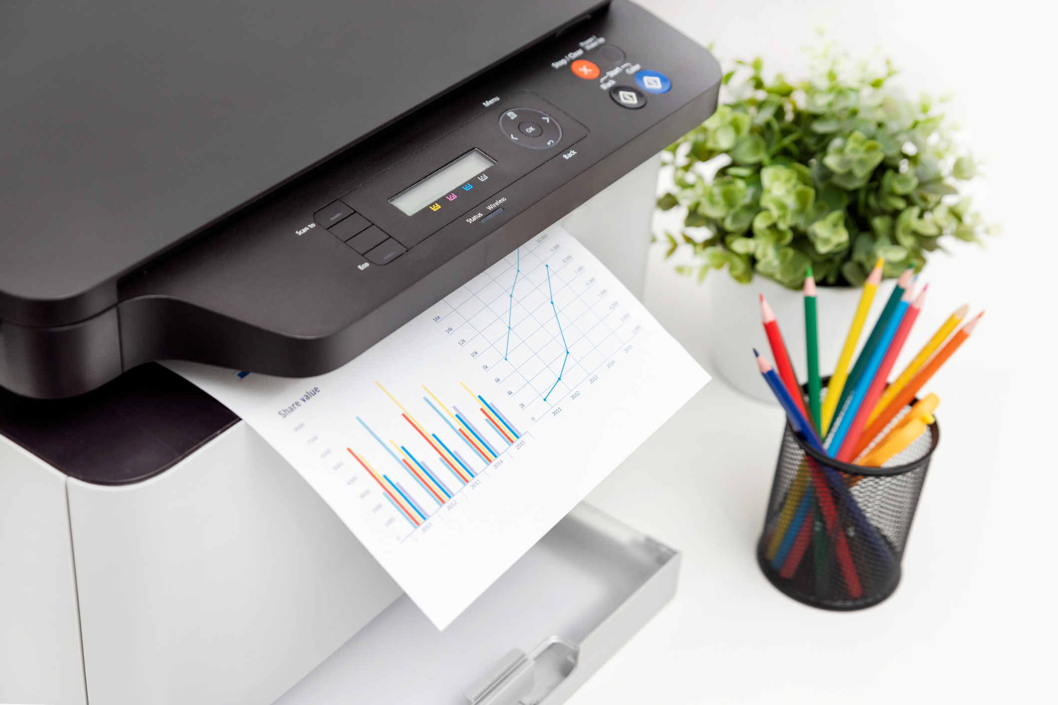 close up of a business printer printing a colorful output of graphs with colored pencils and a plant nearby