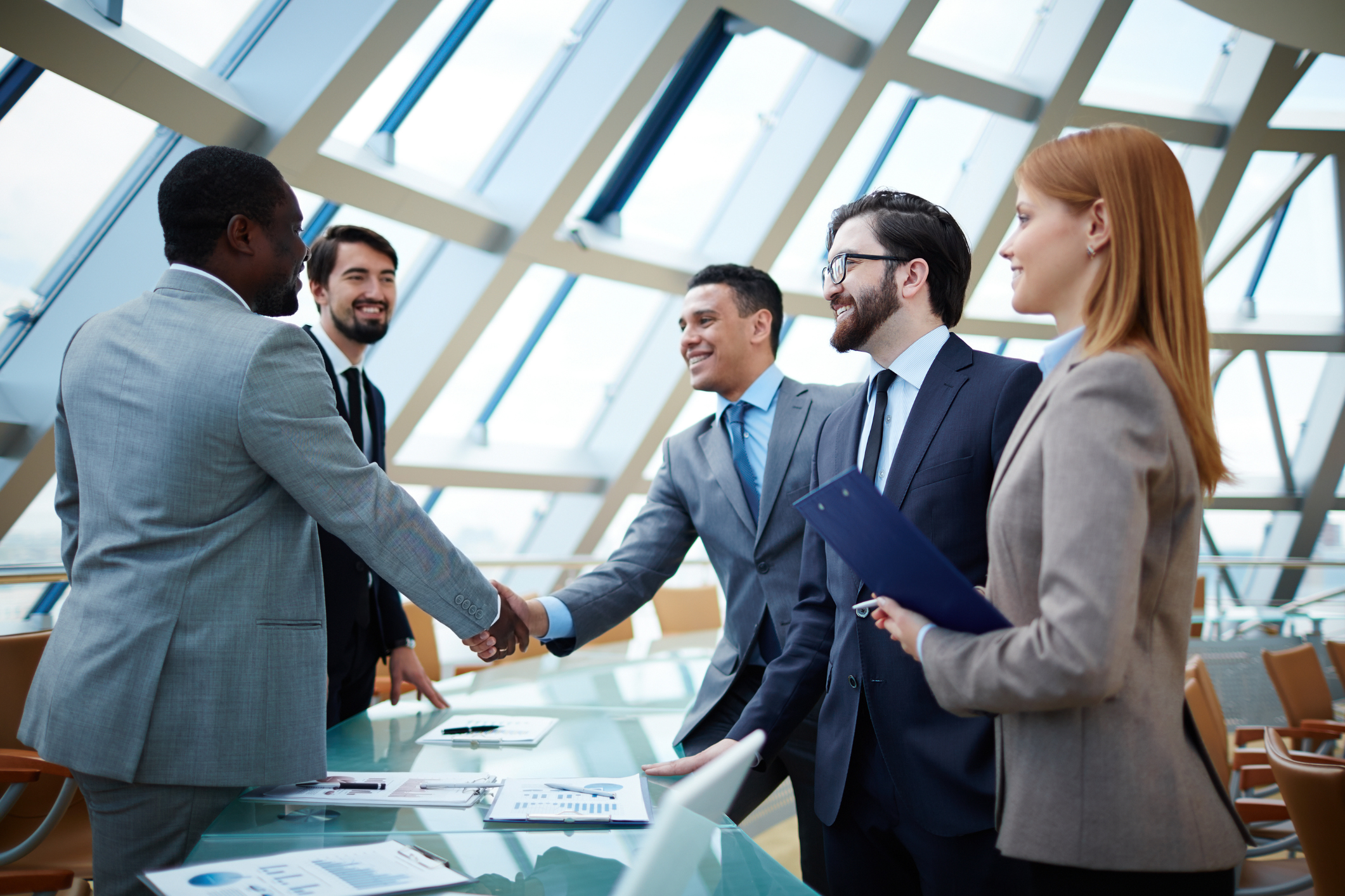 Five business professionals stand around a table, two of which are shaking hands, signifying copier leasing companies