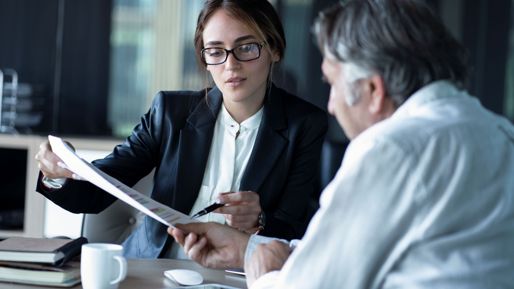 A businesswoman reviews copier lease paperwork with a client holding a pen and pointing out where he should sign.