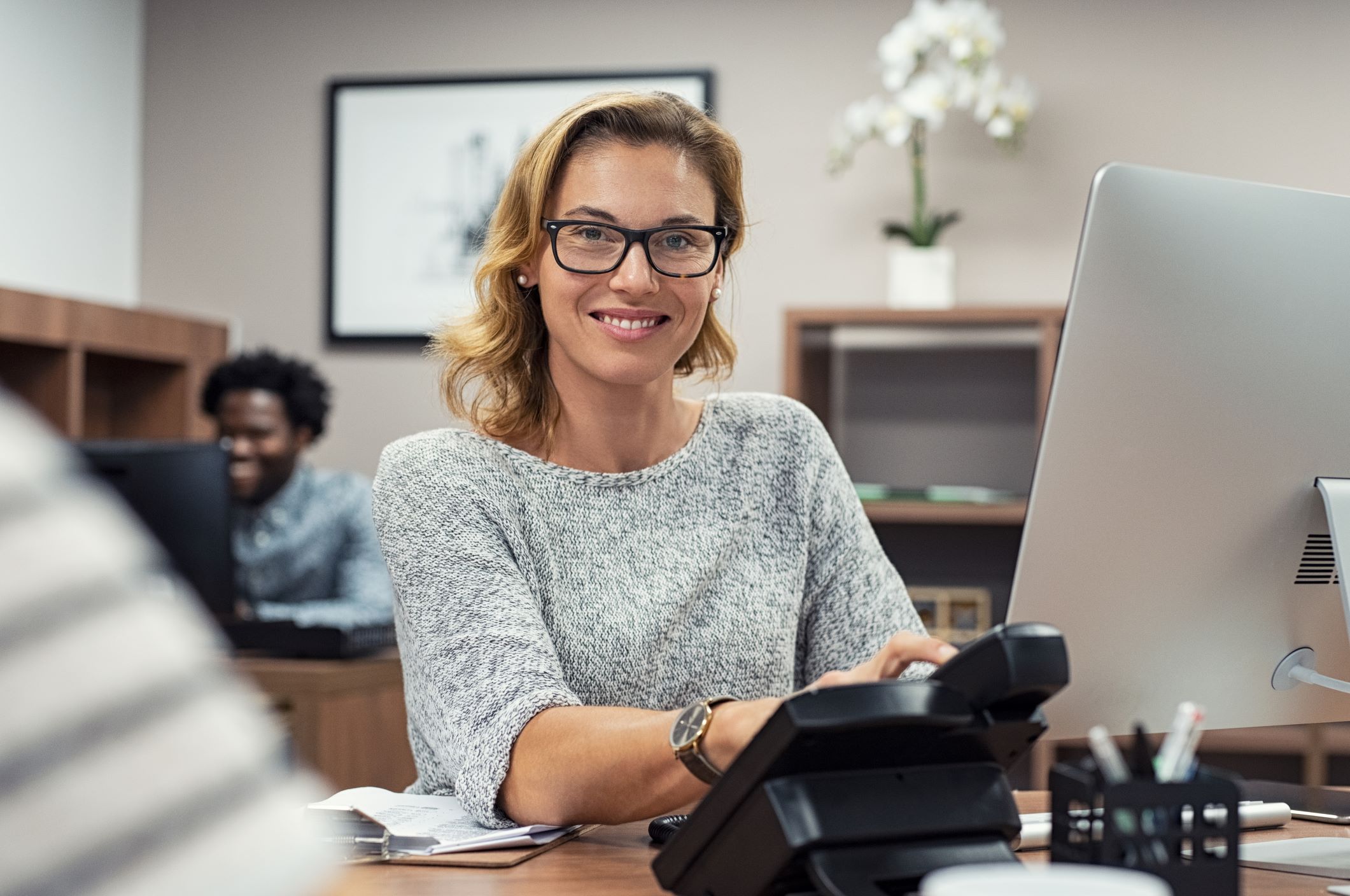 A friendly woman receptionist in the foreground answering an office phone to signify copier service.