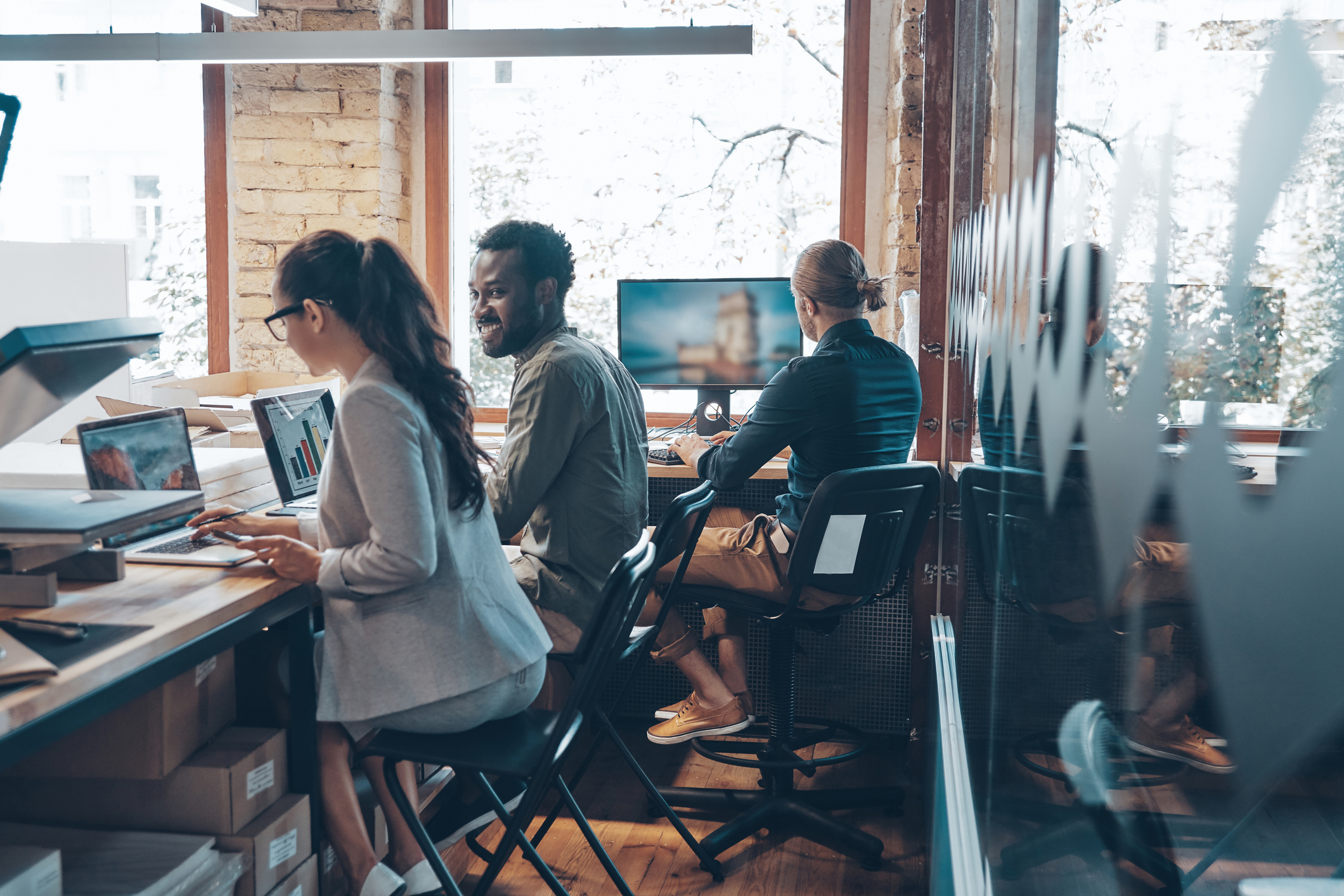 Group of young modern people in smart casual wear communicating and using modern technologies while working in the office signifying an office printer.