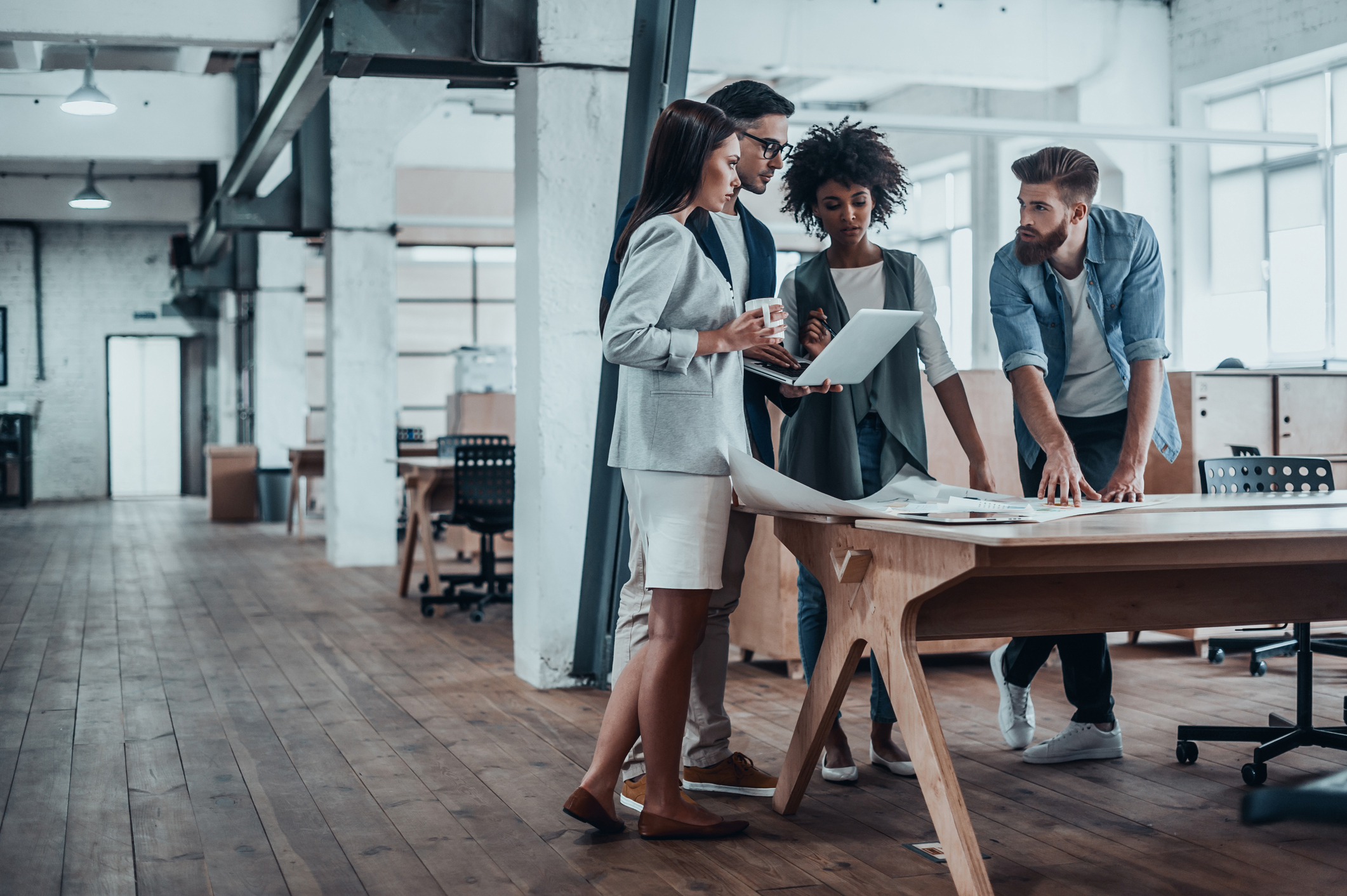 Group of young business people working together in creative office while standing near the wooden desk signifying a printer rental