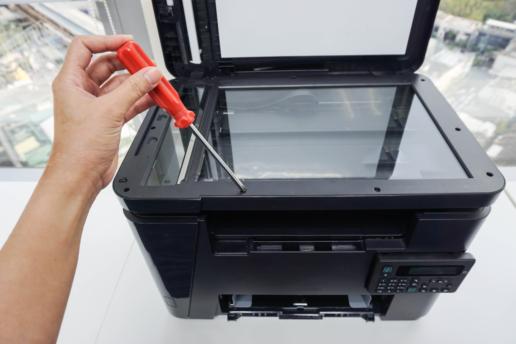 A close up of an office printer where a technician uses a screwdriver on the machine signifying printer service.
