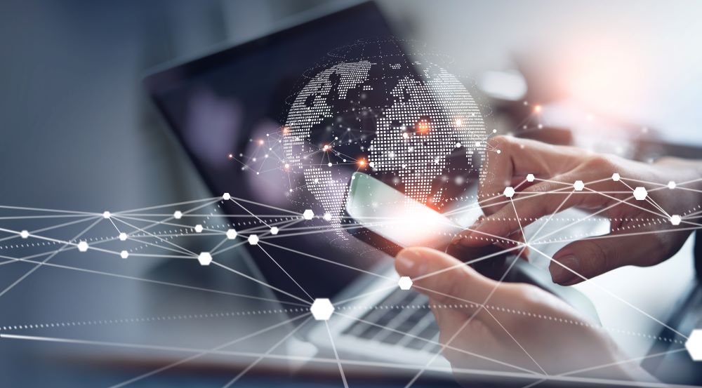 A person uses a smartphone in front of a laptop with a digital globe and network lines overlaid, representing global connectivity and modern VoIP communication technology.