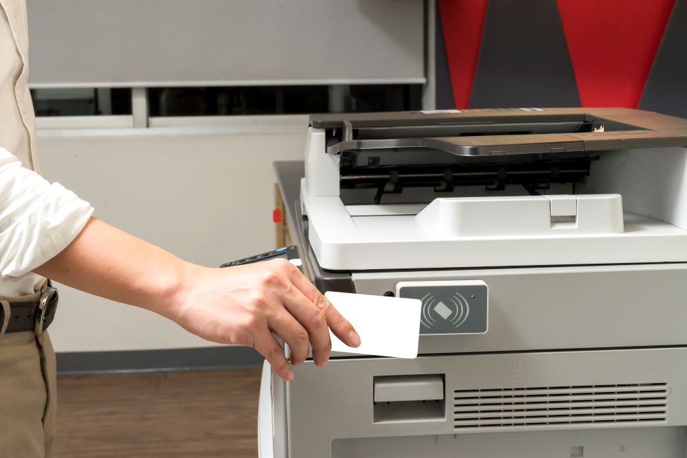 Male office employee scans an ID card at the office printer to release a document signifying secure document printing